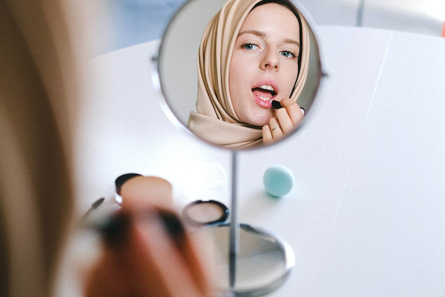 A woman applying lip balm while looking in a small mirror.