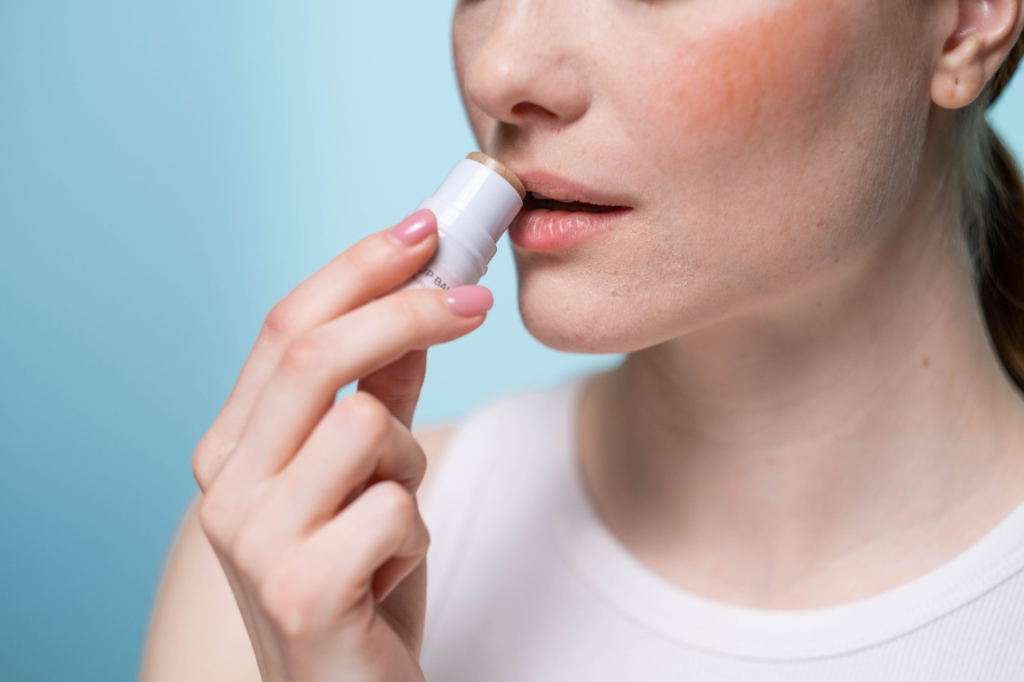 A woman applying a lip balm to her upper lip.