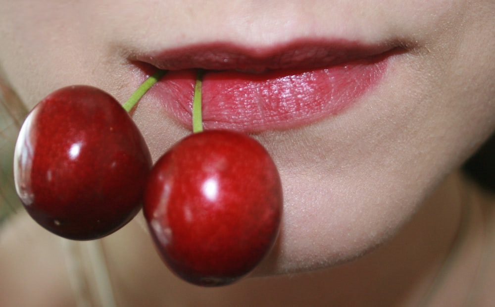  a woman wearing a cherry lip tint while holding cherries with her lips